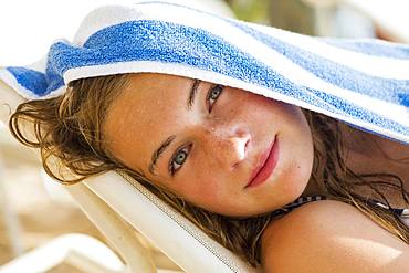 A teenage girl reclining in beach chair with towel on her head, Grand Cayman, Cayman Islands