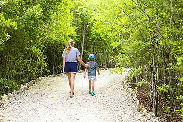 rear view of 13 year old sister and her 5 year old brother walking on nature path, Grand Cayman, Cayman Islands