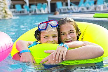 Siblings, brother and sister playing in pool with colorful floaties, Grand Cayman, Cayman Islands