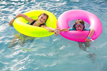 Siblings, brother and sister playing in pool with colorful floaties, Grand Cayman, Cayman Islands