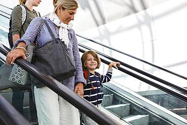 Smiling 5 year old boy traveling on airport escalator with his mother and older sister, Grand Cayman, Cayman Islands