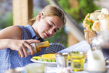 A teenage girl pouring BBQ sauce on ribs and corn, Grand Cayman, Cayman Islands