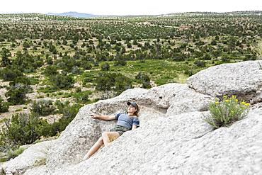 A teenage girl lying down on rock formation at a desert site