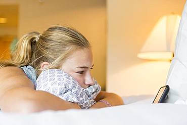 A teenage girl lying on hotel room bed looking at smart phone