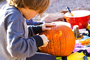 A six year old boy carving pumpkin outdoors at Halloween