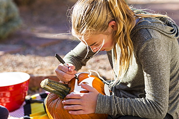 A teenage girl carving pumpkin outdoors at Halloween