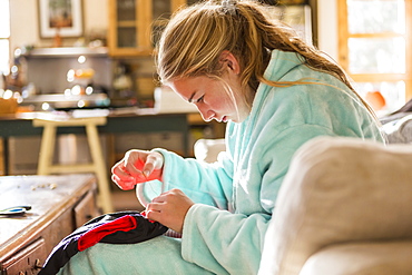 A teenage girl sewing a shirt sitting in her bathrobe