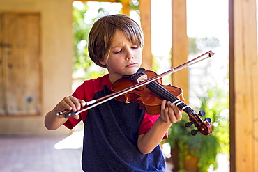 Six year old boy playing violin outside in garden