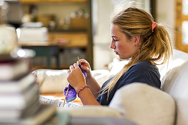 13 year old girl knitting on couch in early morning light