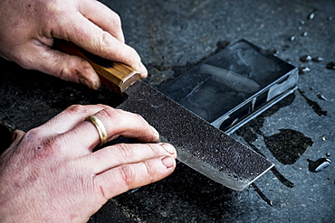 High angle close up of person sharpening handmade knife on a whetstone