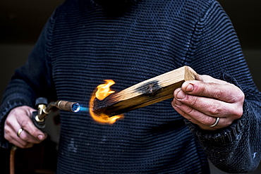 Close up of man holding blowtorch, charring wooden handle of a knife