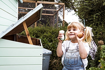 Smiling girl standing outdoors, holding three freshly laid eggs in her hands