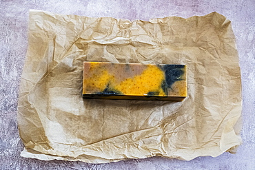 High angle close up of yellow and black homemade bar of soap on brown paper