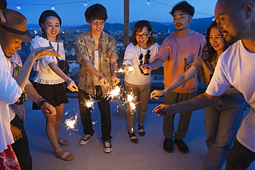 Group of young Japanese men and women with sparklers on a rooftop in an urban setting, Fukuoka, Kyushu, Japan