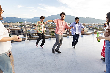 Group of young Japanese men and women dancing on a rooftop in an urban setting, Fukuoka, Kyushu, Japan