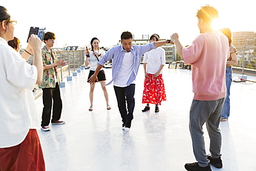 Group of young Japanese men and women dancing on a rooftop in an urban setting, Fukuoka, Kyushu, Japan