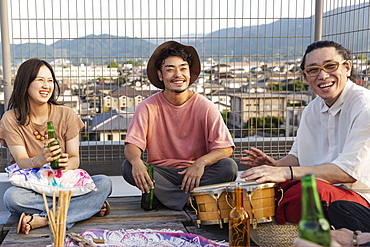 Smiling group of young Japanese men and women sitting on a rooftop in an urban setting, Fukuoka, Kyushu, Japan