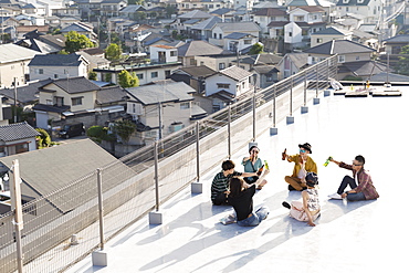 High angle view of group of young Japanese men and women sitting on a rooftop in an urban setting, Fukuoka, Kyushu, Japan