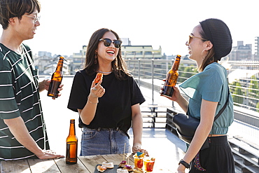 Young Japanese man and two women standing on a rooftop in an urban setting, drinking beer, Fukuoka, Kyushu, Japan