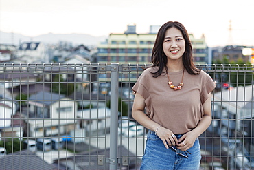 Young Japanese woman standing on a rooftop in an urban setting, looking at camera, Fukuoka, Kyushu, Japan