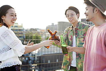 Young Japanese men and woman standing on a rooftop in an urban setting, drinking beer, Fukuoka, Kyushu, Japan