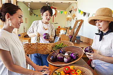 Japanese woman wearing hat working in a farm shop, serving two female customers, Kyushu, Japan