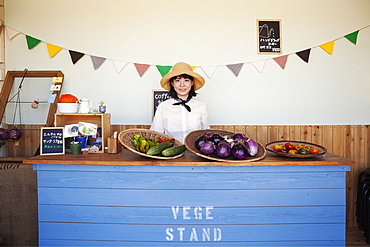 Japanese woman wearing hat standing behind counter in a farm shop, smiling at camera, Kyushu, Japan