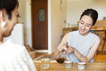 Two Japanese women sitting at a table in a vegetarian cafe, pouring tea, Kyushu, Japan