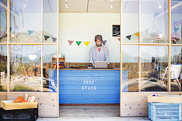 Japanese man wearing cap standing behind counter in farm shop, Kyushu, Japan