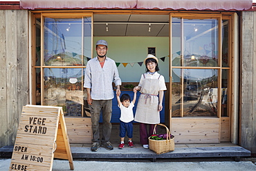 Japanese man, woman and boy standing outside a farm shop, holding hands, looking at camera, Kyushu, Japan