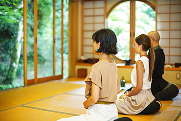 Two Japanese women and Buddhist priest kneeling in Buddhist temple, praying, Kyushu, Japan