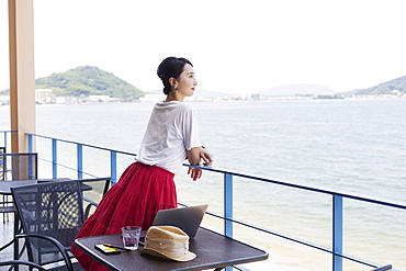 Female Japanese professional standing on balcony of a co-working space, laptop computer on table, Kyushu, Japan