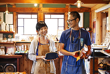 Smiling Japanese woman and man wearing blue apron and glasses standing in a leather shop, Kyushu, Japan