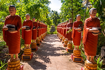 Row of Buddhist monk statues with red robes and alms bowls in the gardens of the Buddhist Temple at Siem Reap, Cambodia