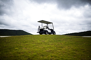 Golf cart parked on the green of a golf course under a cloudy sky, Vietnam