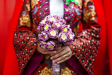 Close up of young Vietnamese bride wearing a colourful robe, holding a bouquet of lotus flowers, Vietnam, Mekong Delta