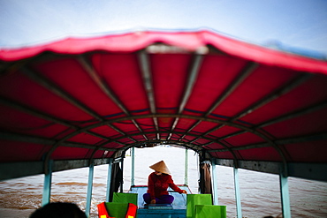 Woman piloting a boat with red canopy through a river, Vietnam, Mekong Delta