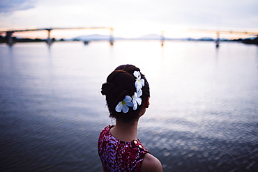 Rear view of woman with flowers in her hair, standing by the sea at sunset, bridge in the distance, Vietnam