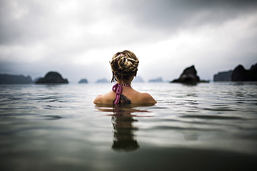 Rear view of woman with blond braided hair wading into the ocean, Vietnam