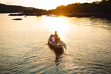 High angle view of man piloting a small boat toward an island at sunrise, Vietnam