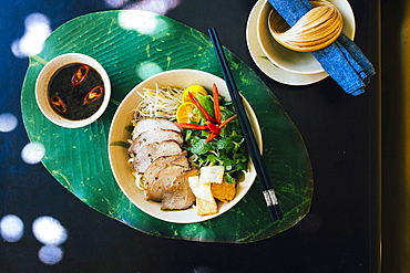 High angle close up of bowl of Cao Lau noodles with grilled pork and herbs, Vietnam