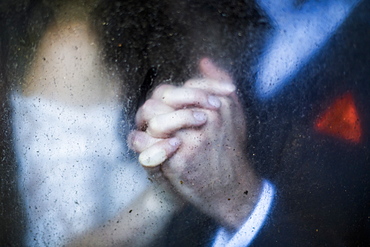 Close up through dirty window of couple holding hands