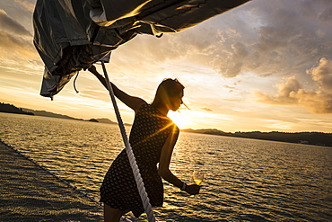 Woman holding wine glass standing on board a boat, sunset dinner cruise on Indian Ocean, Malaysia