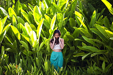Young woman standing in rain forest with lush green foliage, Thailand