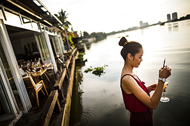 Woman drinking ginger-lemongrass martini at a bar on the banks of a river, Vietnam