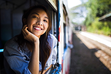 Smiling young woman riding on a train, looking out of window, Myanmar