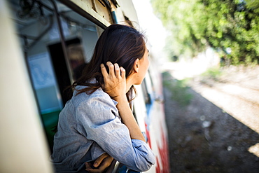 Young woman riding on a train, looking out of window, Myanmar