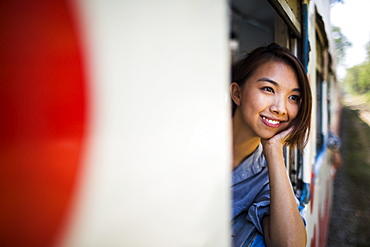 Smiling young woman riding on a train, looking out of window, Myanmar