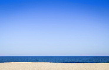 An empty sandy beach and ocean, view out to sea under a clear blue sky, Portugal