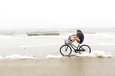 A teenage girl biking on sand on a beach, St Simon's Island, Georgia, United States